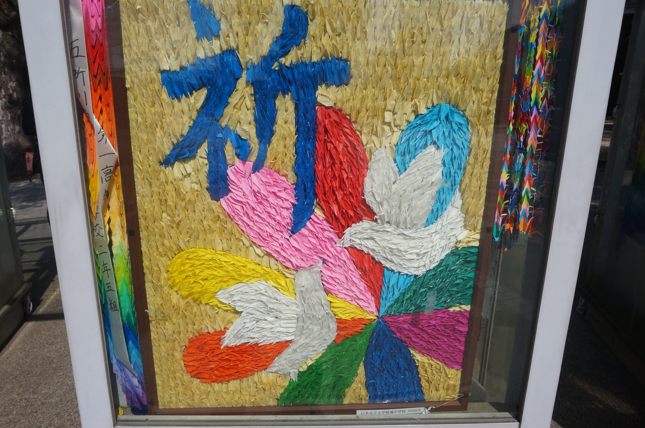 Ein Bild aus Origami-Kranichen. Das Kanji darauf bedeutet "Gebet" oder auch "beten".