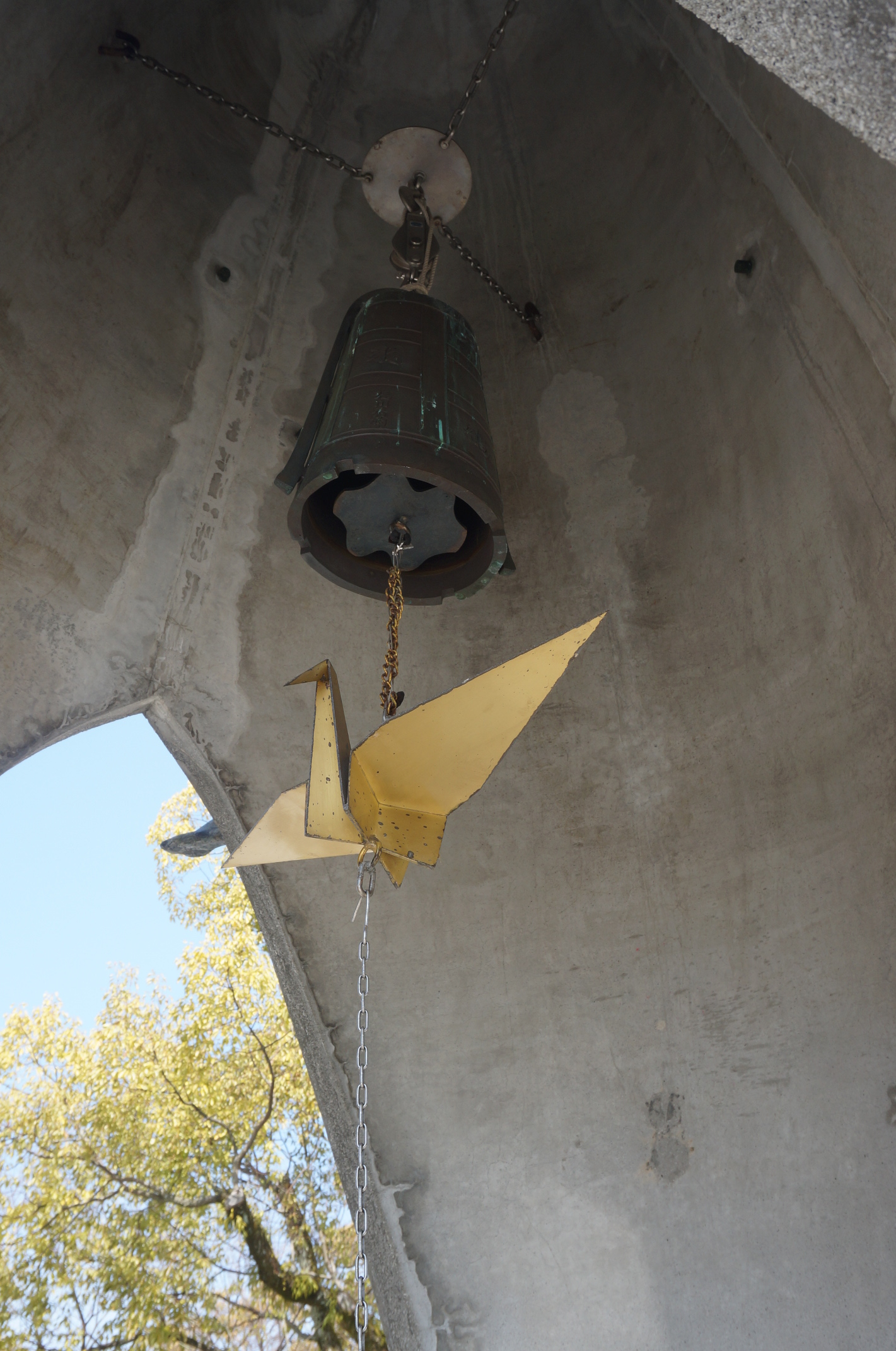 Kranich mit Glocke unter Kindermonument.